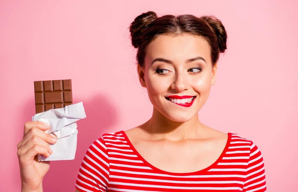 women in front of pink wall looking excitedly at a chocolate bar
